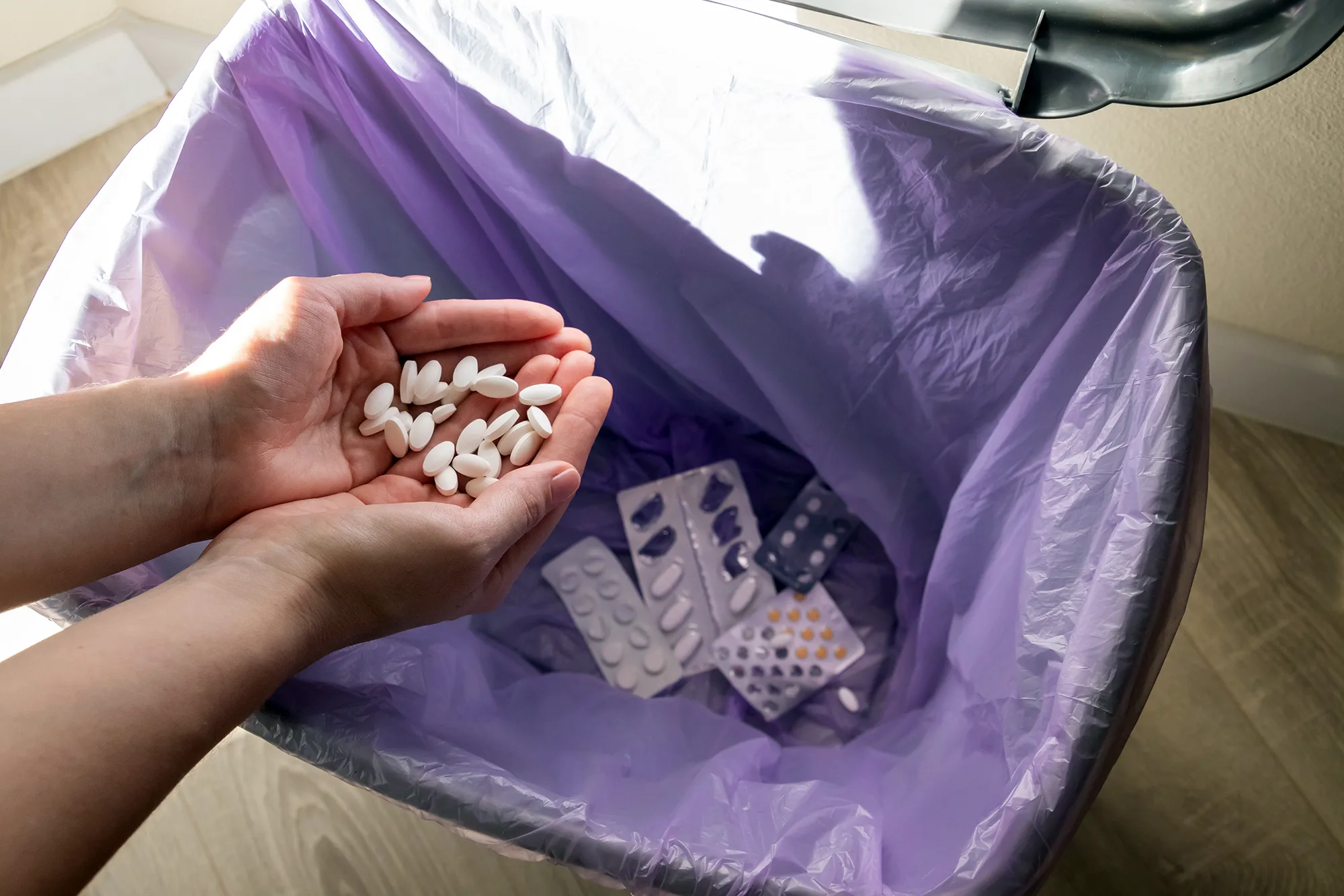 Photo of a pair of hands, full of pills, hovering over a trash can.