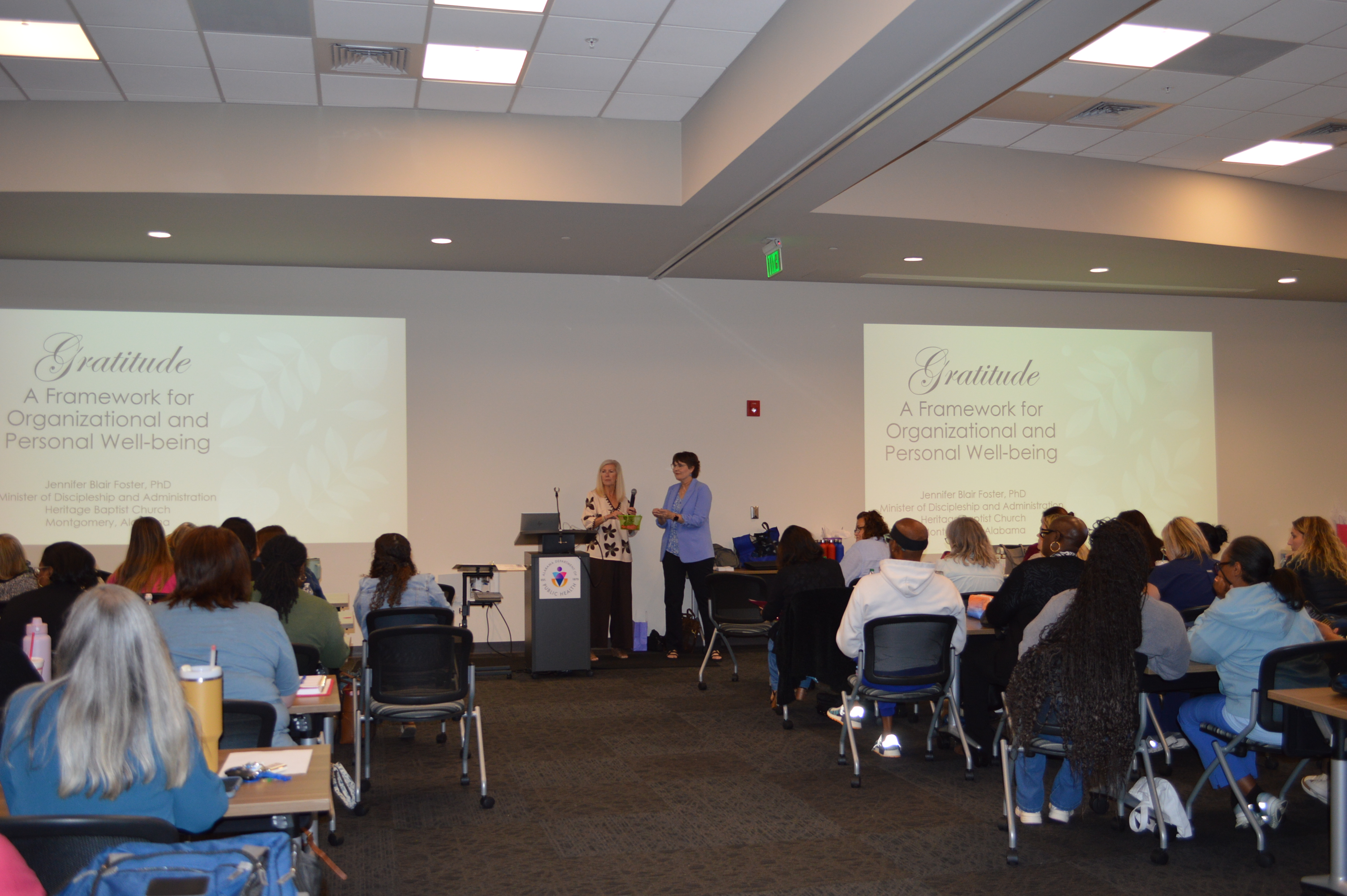 Two women stand at a podium in front of conference attendees.